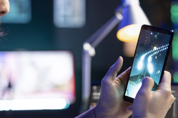 Male gamer sitting at desk and playing space shooter video games on smartphone. Man streaming online videogames for e-sport tournament on his mobile device while resting from work.